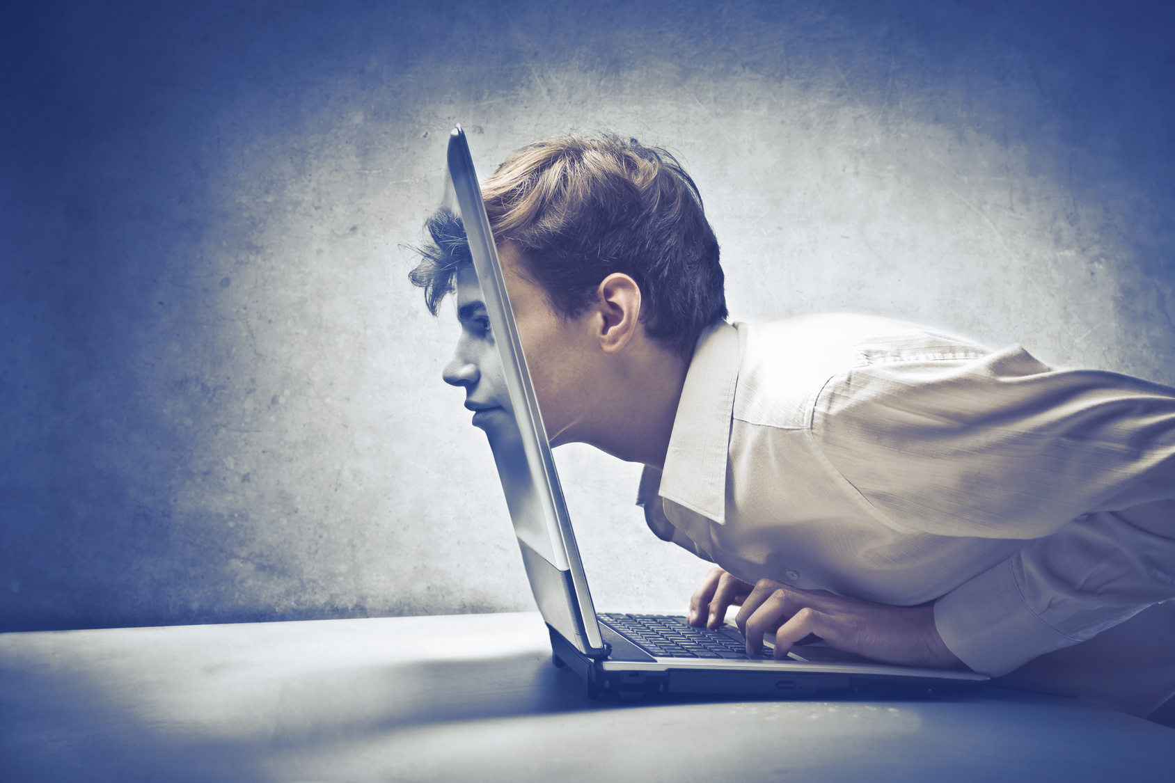 A man leans forward with his face merging into a laptop screen, suggesting deep immersion or absorption in technology.