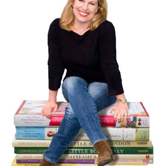 A woman with blonde hair, wearing a black top and blue jeans, sits smiling on a stack of large, colorful books against a white background.